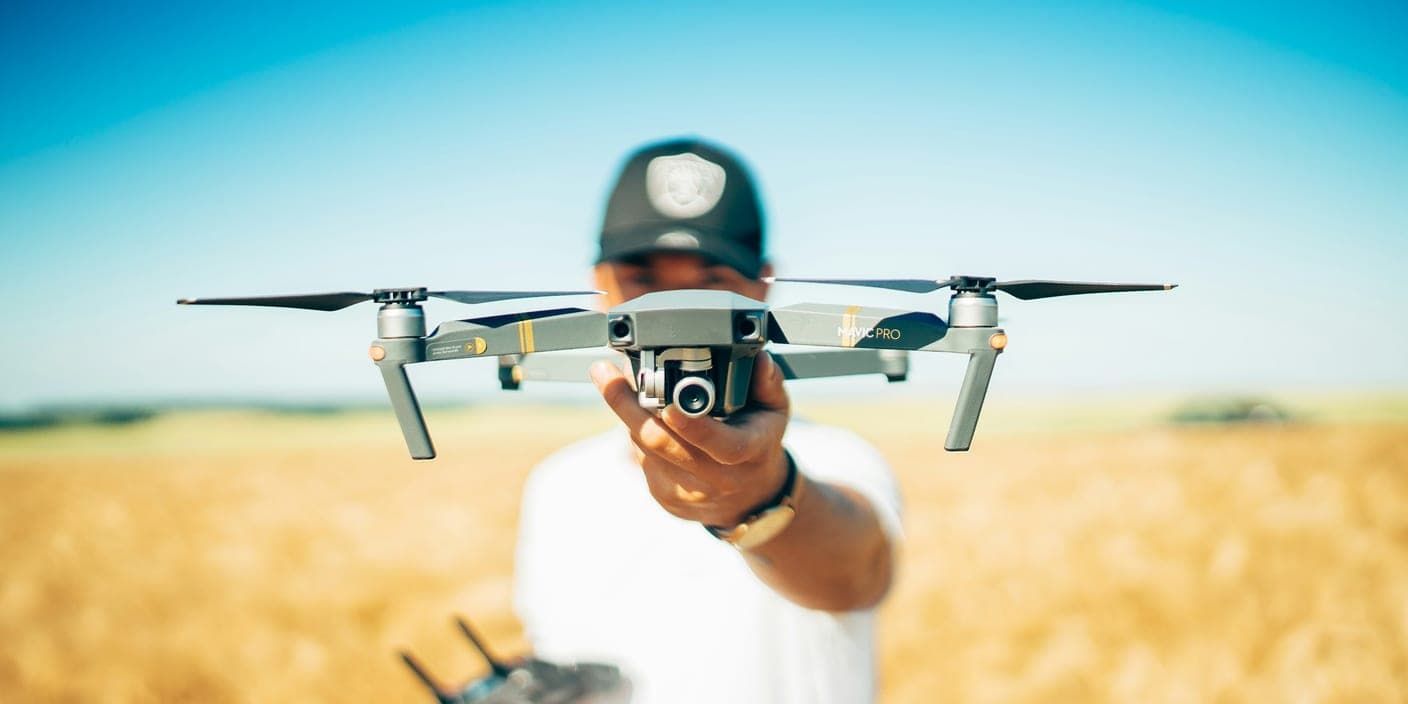 A pilot holding up a camera drone in front of a wheat field