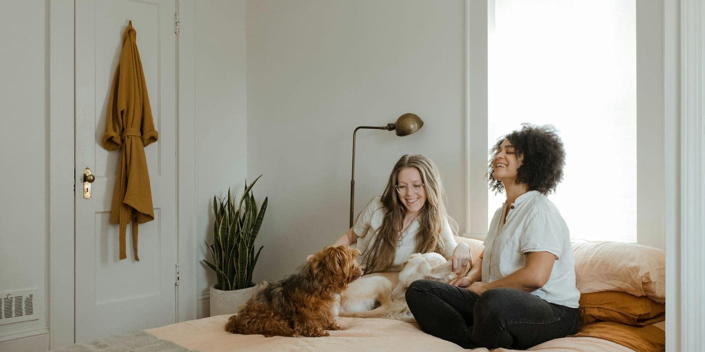 Two people sitting on a bed at home with a small brown dog